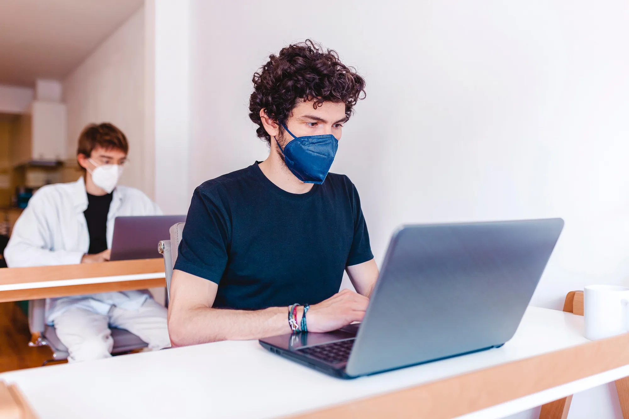 Two men wearing protective masks working on their laptop at office